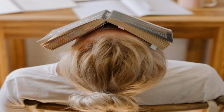 Ragazza delle scuole superiori con dei libri sulla testa.